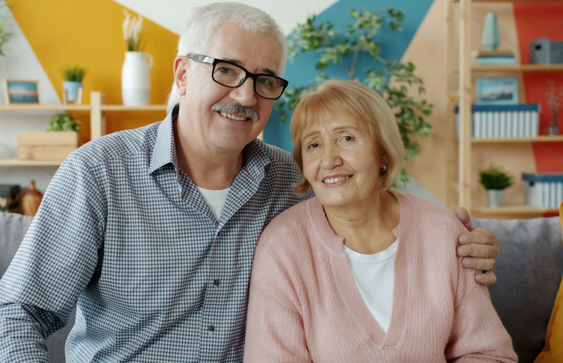 Casal de idosos sorrindo em casa, representando quem contrata plano de saude depois dos 60 anos